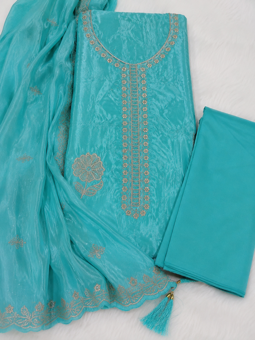 Turquoise blue ethnic wear set featuring a heavily embroidered kurta, matching trousers, and a sheer dupatta with gold zari embroidery, laid out on a white textured background.